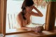 A woman sitting at a window with a coconut in her hand.