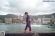 A woman in a purple track suit and orange shoes standing on a wall by the water.