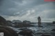 A naked woman standing on a rocky beach next to the ocean.